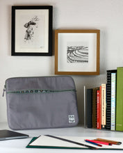 Cargar imagen en el visor de la galería, A grey 15 inch laptop case sits on a white table with pencils and a sketchpad ready for use. On the white wall behind are some pen and ink drawings of the shells on the sea shore and a snowy field with tractor markings.
