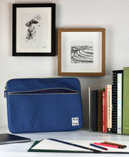 이미지를 갤러리 뷰어에 로드 , A 15 inch MacBook case in blue shade shows the patterned lining inside the pocket as it sits on a desk next to a row of sketchbooks and design manuals.
